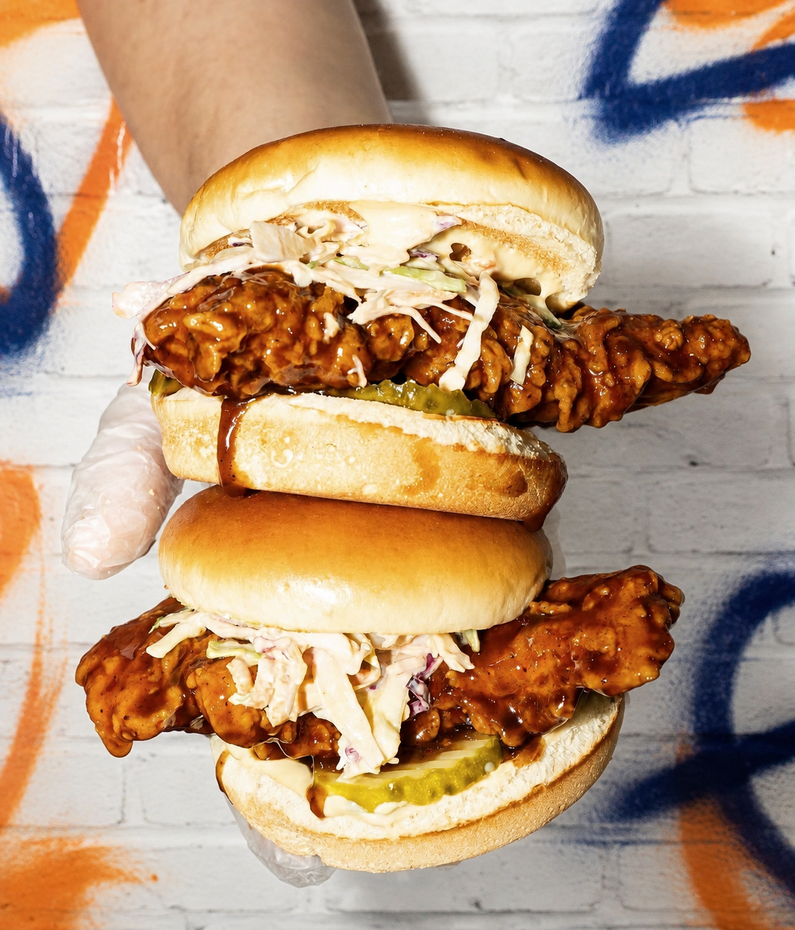 Atomic Wings crispy chicken sandwiches on a white graffiti brick background