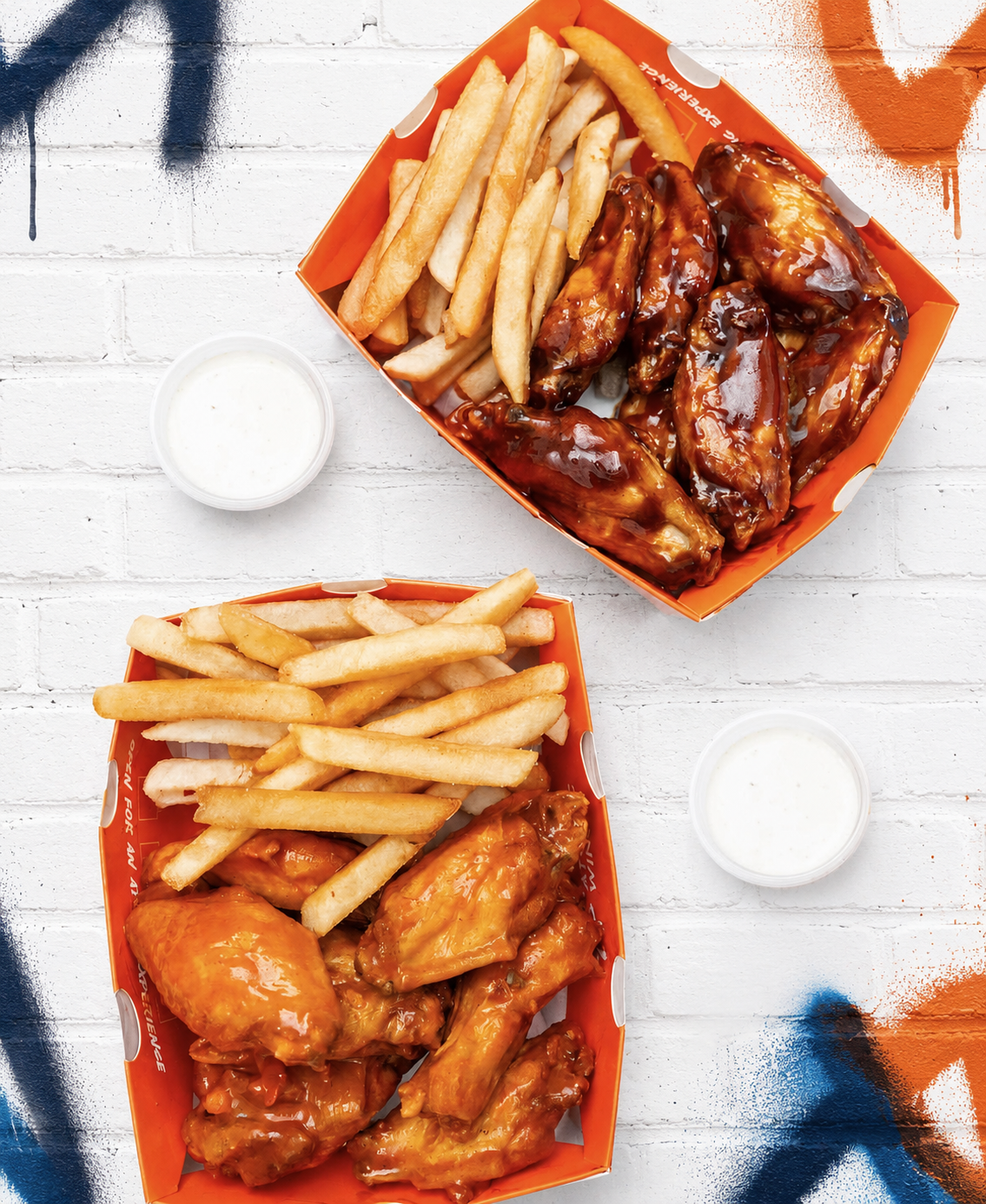 Atomic Wings sauced wings and fries on a white graffiti brick background